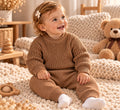 Baby trägt ein zweiteiliges Strick-Set mit Pullover und Hose in Braun