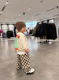 Kind im Oversize-Set mit beiger Sweatshirtjacke und Schachbretthose, Rückansicht mit „Ride Big Waves“-Print, dazu braune Strickmütze