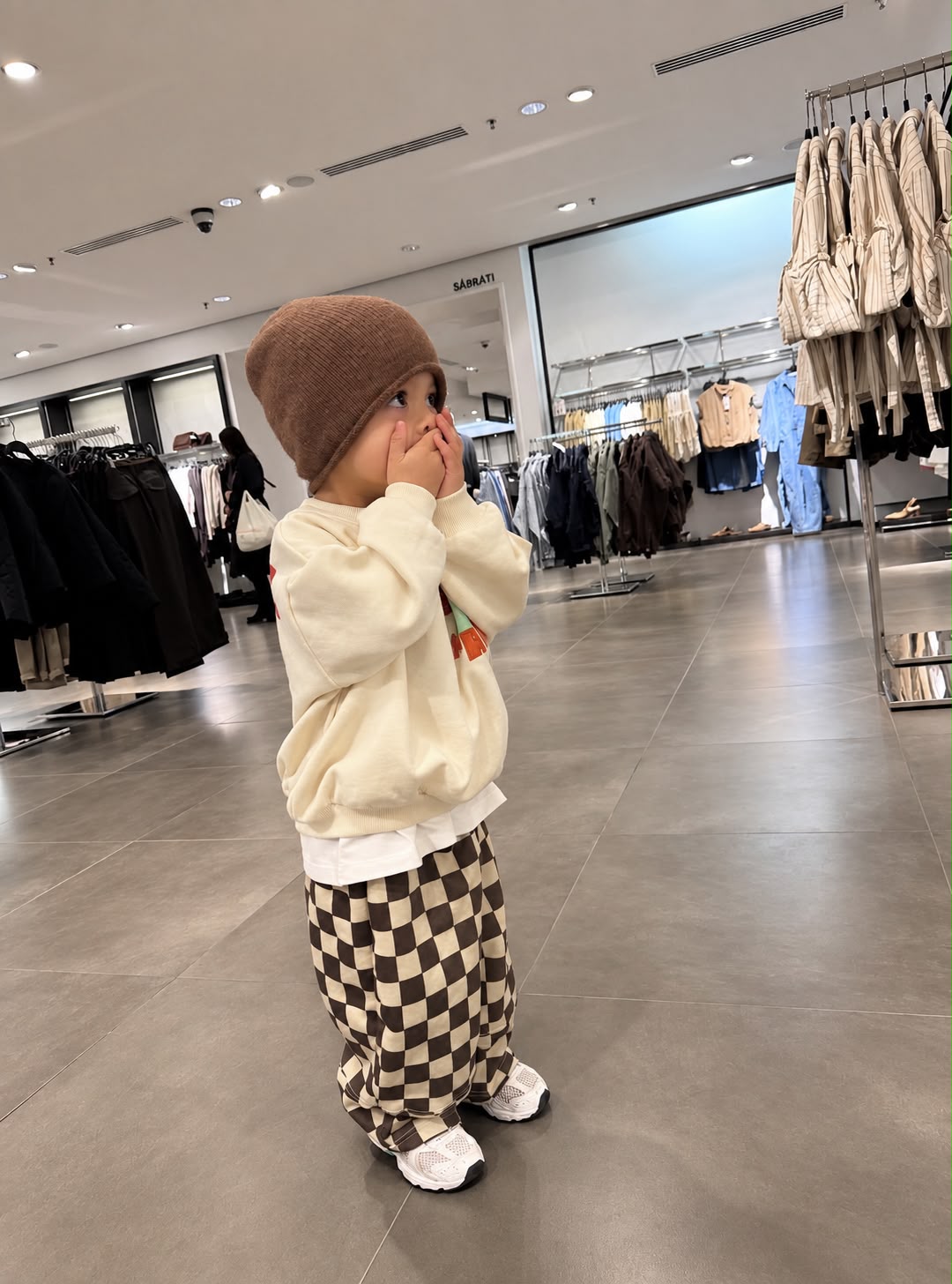 Kind von vorne im Oversize-Sweater mit „Ride Big Waves“-Print und schwarz-weißer Schachbretthose