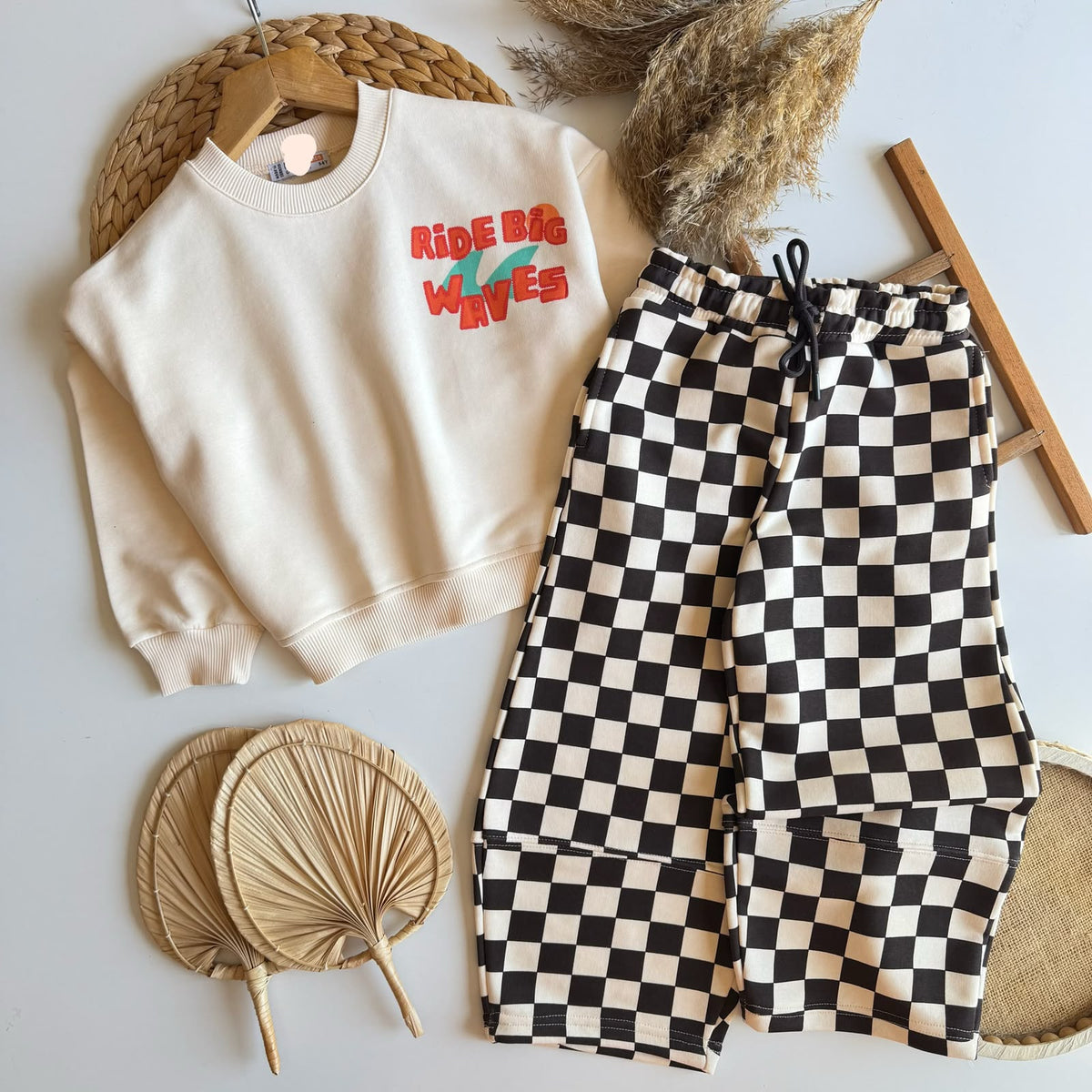2-teiliges Kinder-Set mit cremefarbenem Sweater und schwarz-weißer Schachbretthose, flach liegend fotografiert