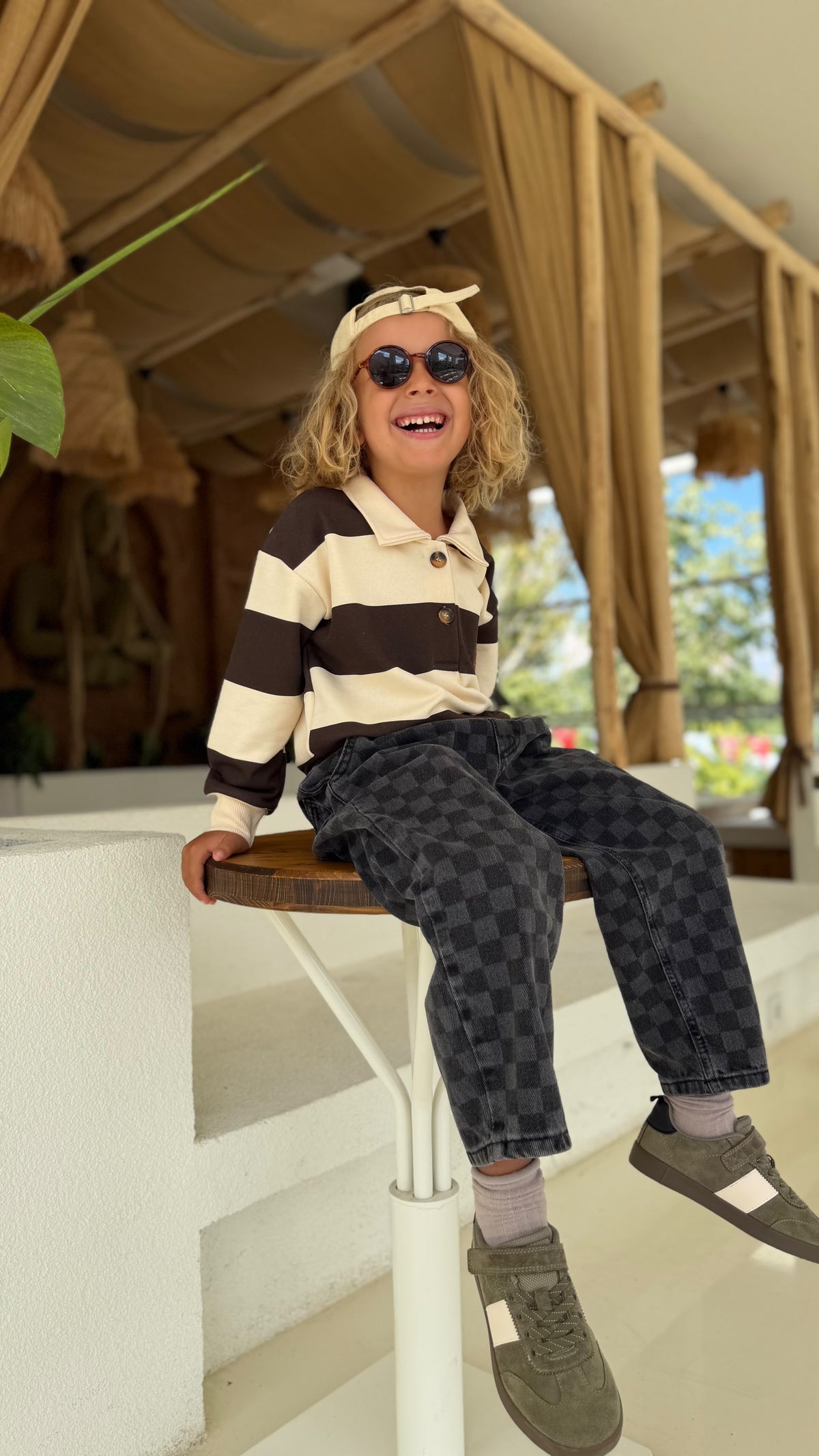 Kind auf einem Hocker im Teddy-Check-Kinder-Set mit Cap und Sonnenbrille