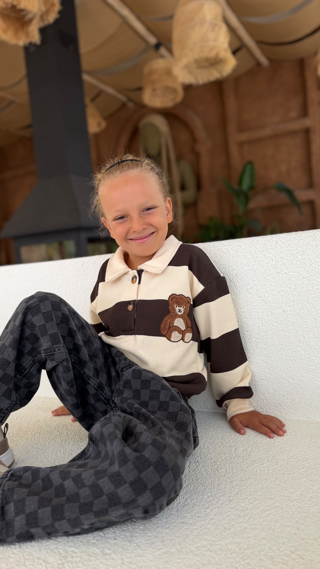 Kind lächelnd im gestreiften Kinder-Set mit Teddy-Patch und dunkler Karohose