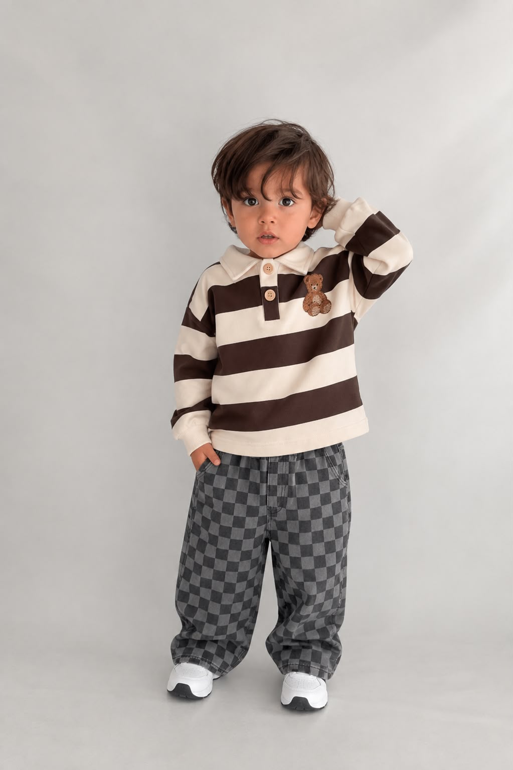 Kleinkind im Teddy-Check-Kinder-Set mit gestreiftem Oberteil mit Teddy-Patch und grauer Karohose, Studioshotaufnahme