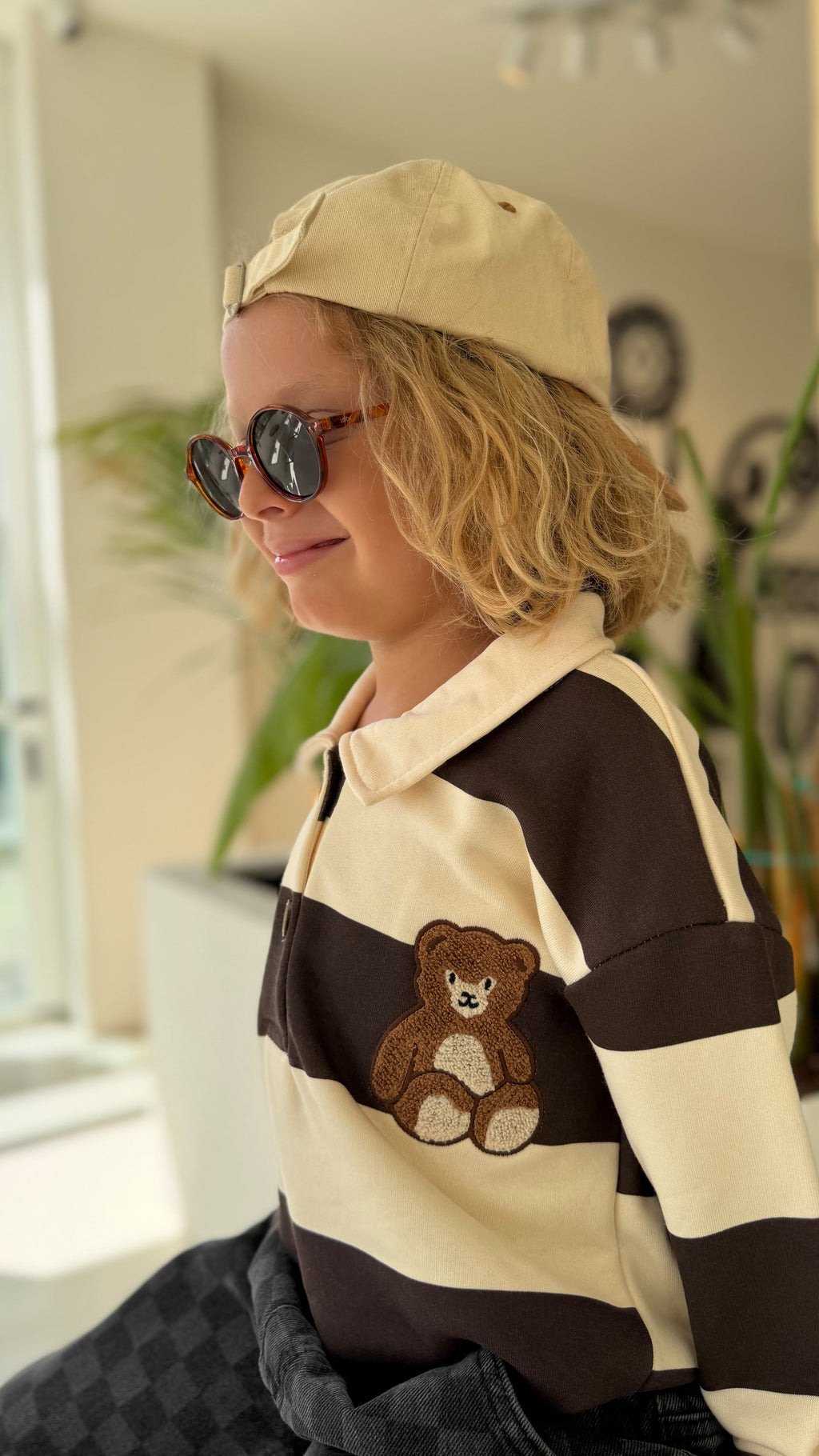 Nahaufnahme des gestreiften Kinder-Oberteils mit Teddy-Patch, dazu beige Cap und Sonnenbrille