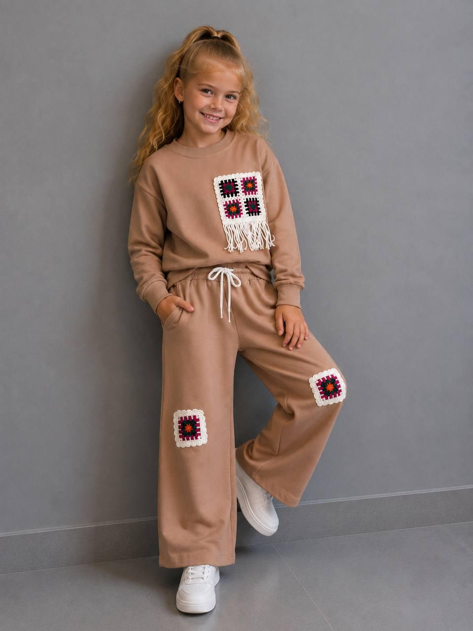 Crochet Vibes Kids Set in Hellbraun: Sweater mit Häkel-Applikation und Fransen, weite Hose mit Häkel-Patches, getragen mit weißen Sneakern.