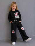 Crochet Vibes Kids Set in Schwarz: Sweater mit Häkel-Applikation und Fransen, weite Hose mit Häkel-Patches, getragen mit weißen Sneakern.