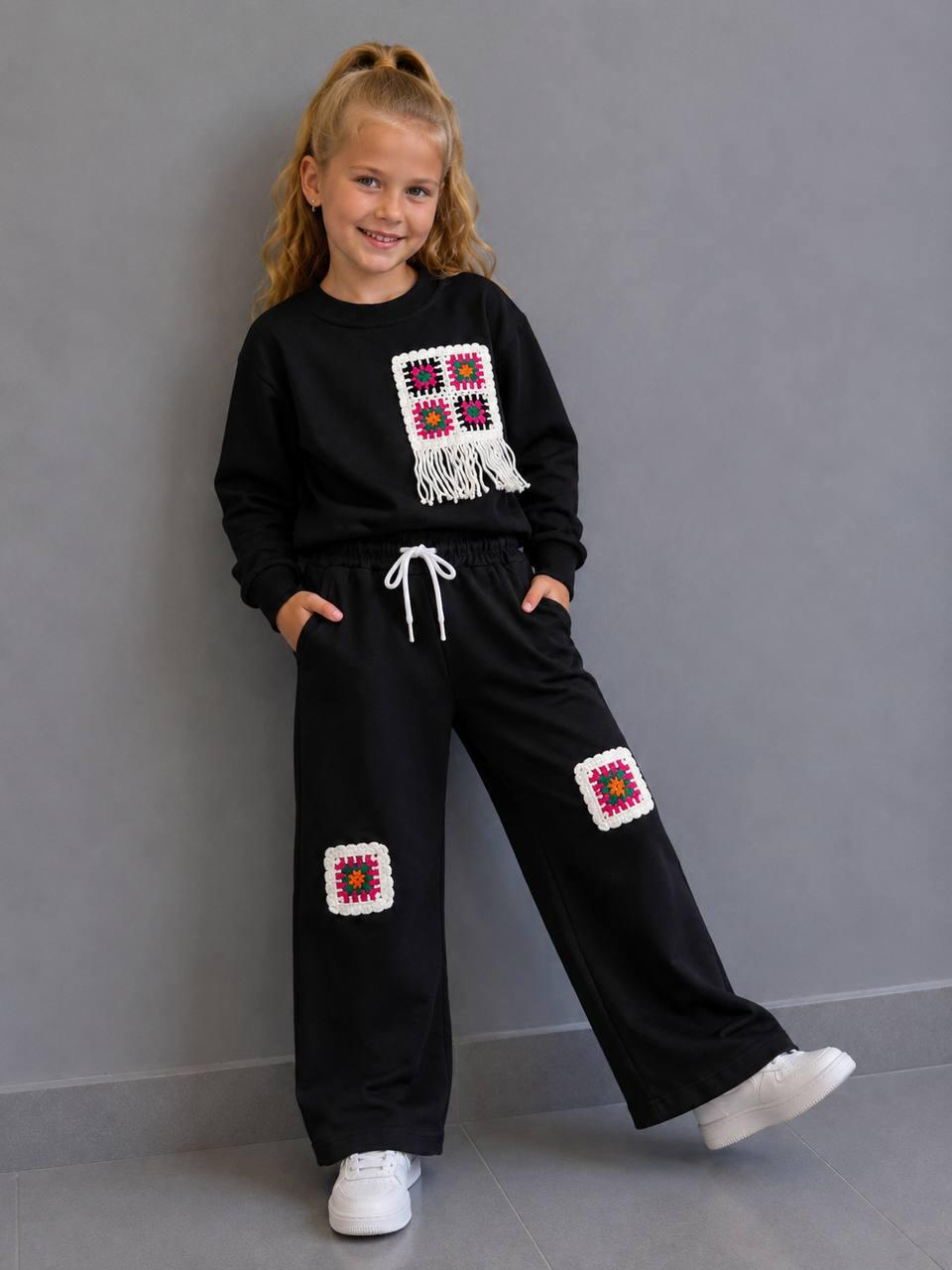 Crochet Vibes Kids Set in Schwarz: Sweater mit Häkel-Applikation und Fransen, weite Hose mit Häkel-Patches, getragen mit weißen Sneakern.