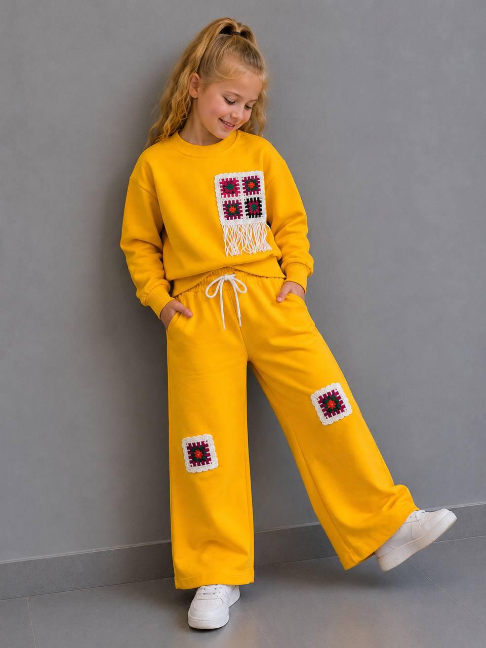 Crochet Vibes Kids Set in Gelb: Sweater mit Häkel-Applikation und Fransen, weite Hose mit Häkel-Patches, getragen mit weißen Sneakern.
