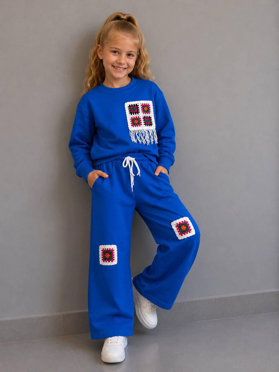 Crochet Vibes Kids Set in Blau: Sweater mit Häkel-Applikation und Fransen, weite Hose mit Häkel-Patches, getragen mit weißen Sneakern.