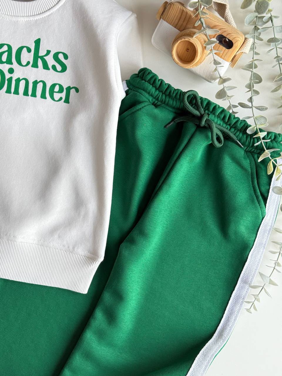  Nahaufnahme des 2-teiligen Kinder-Sets mit weißem Sweatshirt mit „Snacks for Dinner“-Print und grüner Hose mit Kontraststreifen