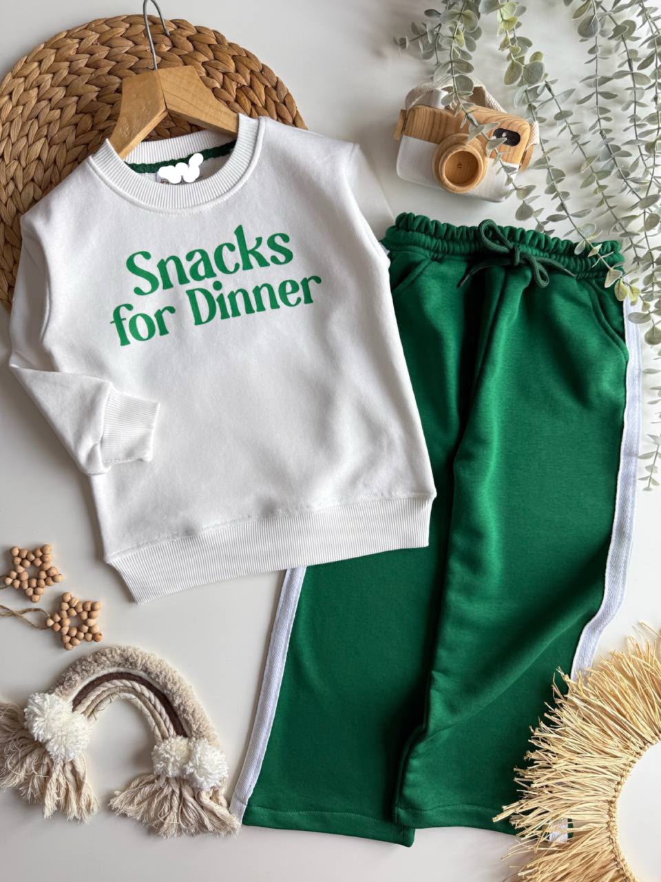 2-teiliges Kinder-Set mit weißem Sweatshirt mit „Snacks for Dinner“-Print und grüner Hose, flach liegend fotografiert