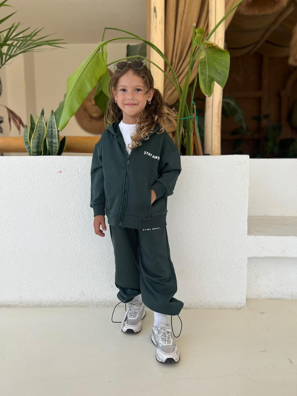 Mädchen mit Sonnenbrille im dunkelgrünen Stay-Kind-Kinder-Set aus Zip-Hoodie-Jacke und weiter Hose im Freien