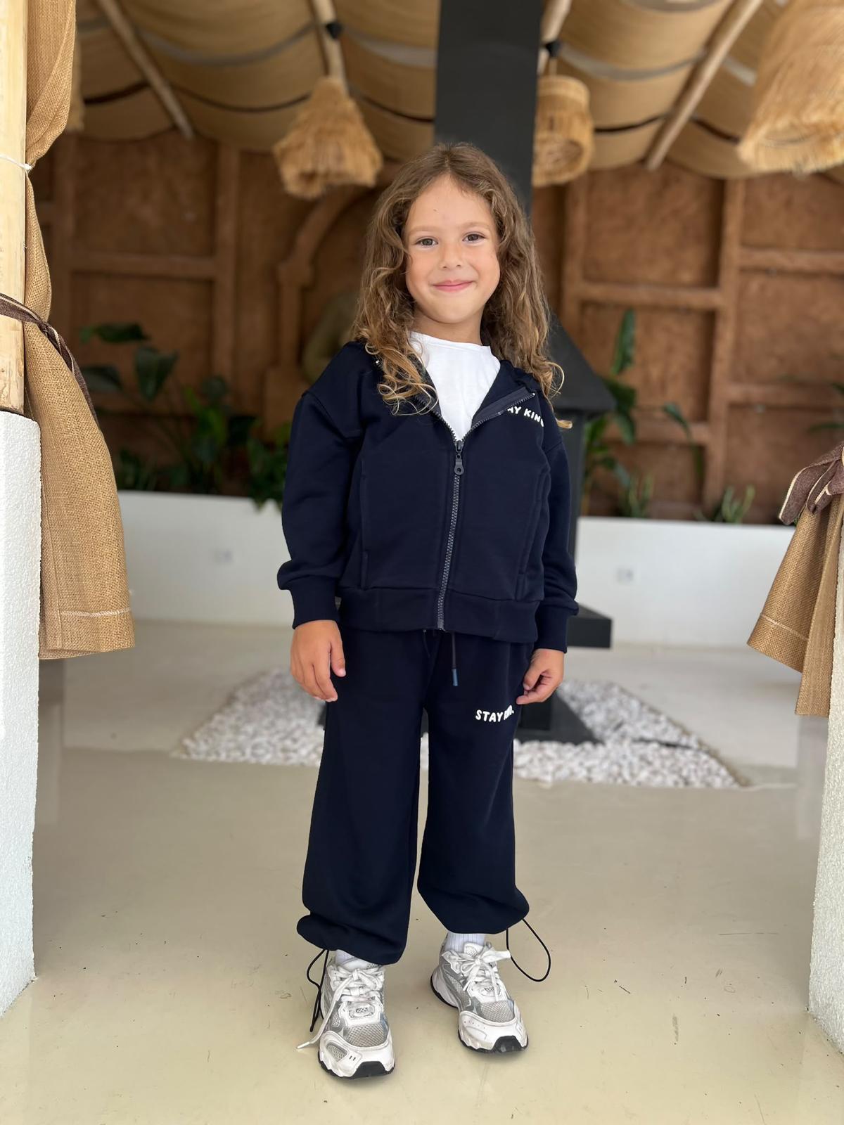 Mädchen lächelnd im dunkelblauen Stay-Kind-Kinder-Set aus Zip-Hoodie-Jacke mit Kapuze und weiter Hose