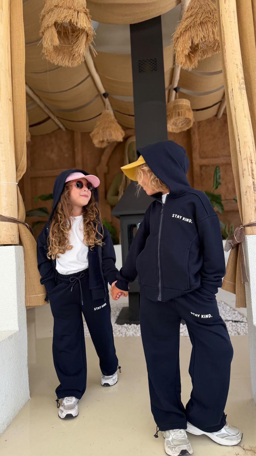 Zwei Kinder im dunkelblauen Stay-Kind-Kinder-Set aus Zip-Hoodie-Jacke und weiter Hose, Hand in Hand