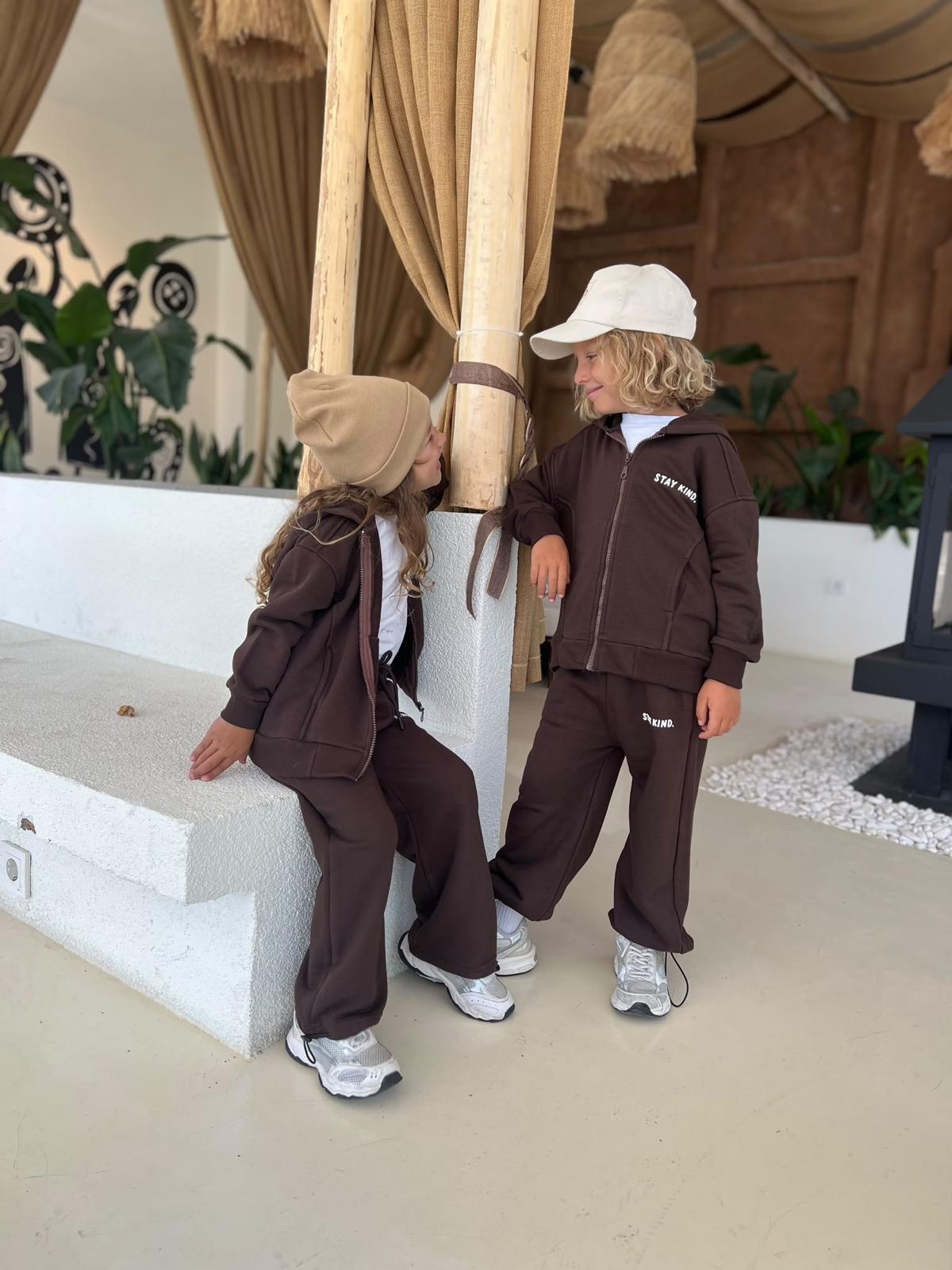 Zwei Kinder im dunkelbraunen Stay-Kind-Kinder-Set aus Zip-Hoodie-Jacke und weiter Hose im Freien