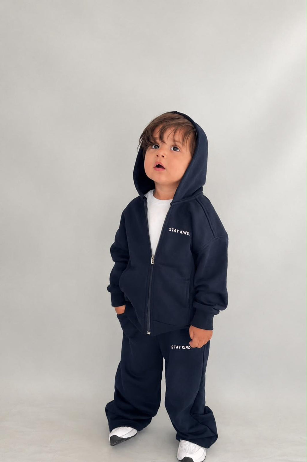 Kleinkind im dunkelblauen Stay-Kind-Kinder-Set aus Zip-Hoodie-Jacke mit Kapuze und weiter Hose mit „Stay Kind“-Print