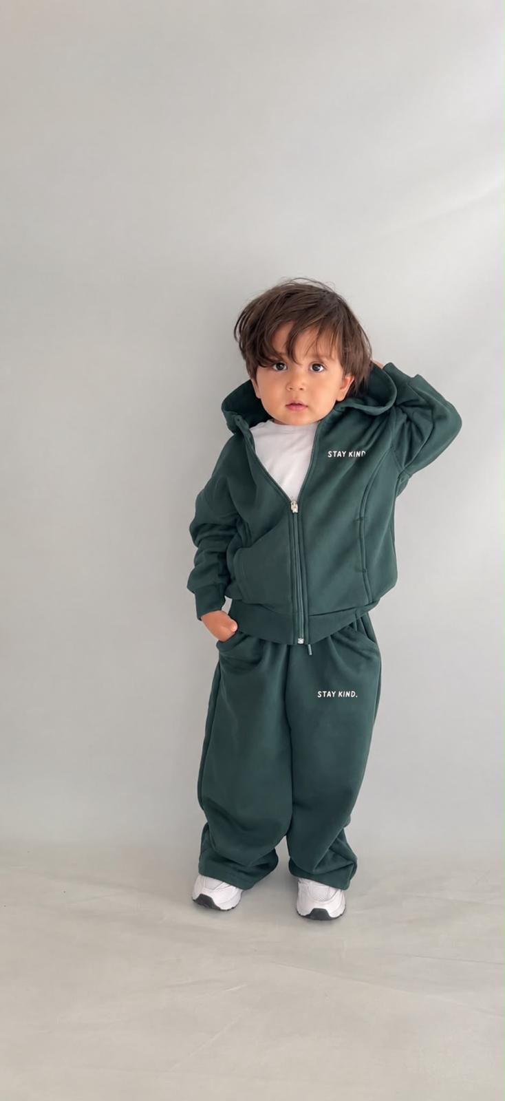 Mädchen im dunkelgrünen Stay-Kind-Kinder-Set aus Zip-Hoodie-Jacke mit Kapuze und weiter Hose mit „Stay Kind“-Print