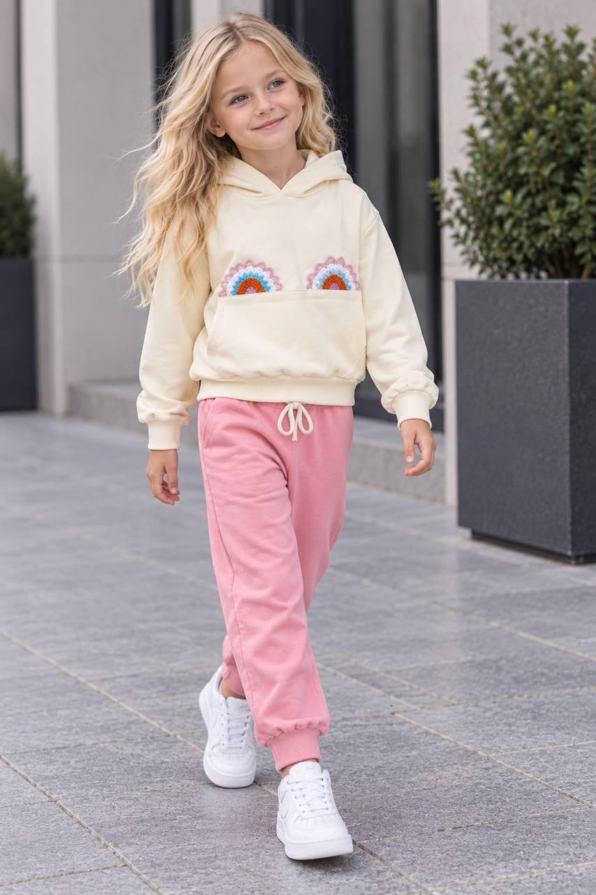 Mädchen trägt das Rainbow Love Set mit cremefarbenem Regenbogen-Hoodie und rosa Hose mit Kordelzug.