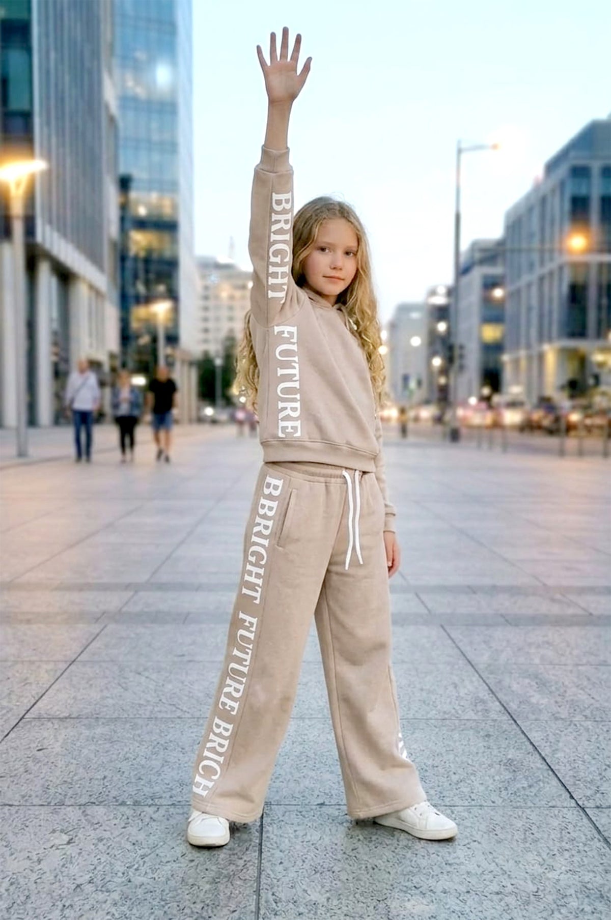 Bright Future Kids Set in Beige: gefütterter Sweater und weite Hose mit Bright-Future-Schriftzug entlang des Ärmels und Hosenbeins, getragen mit weißen Sneakern.
