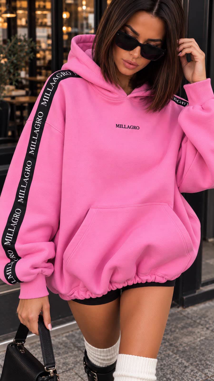 Oversize Hoodie Millagro in Pink mit schwarzen Logo-Bändern an den Ärmeln, getragen mit Shorts und Boots