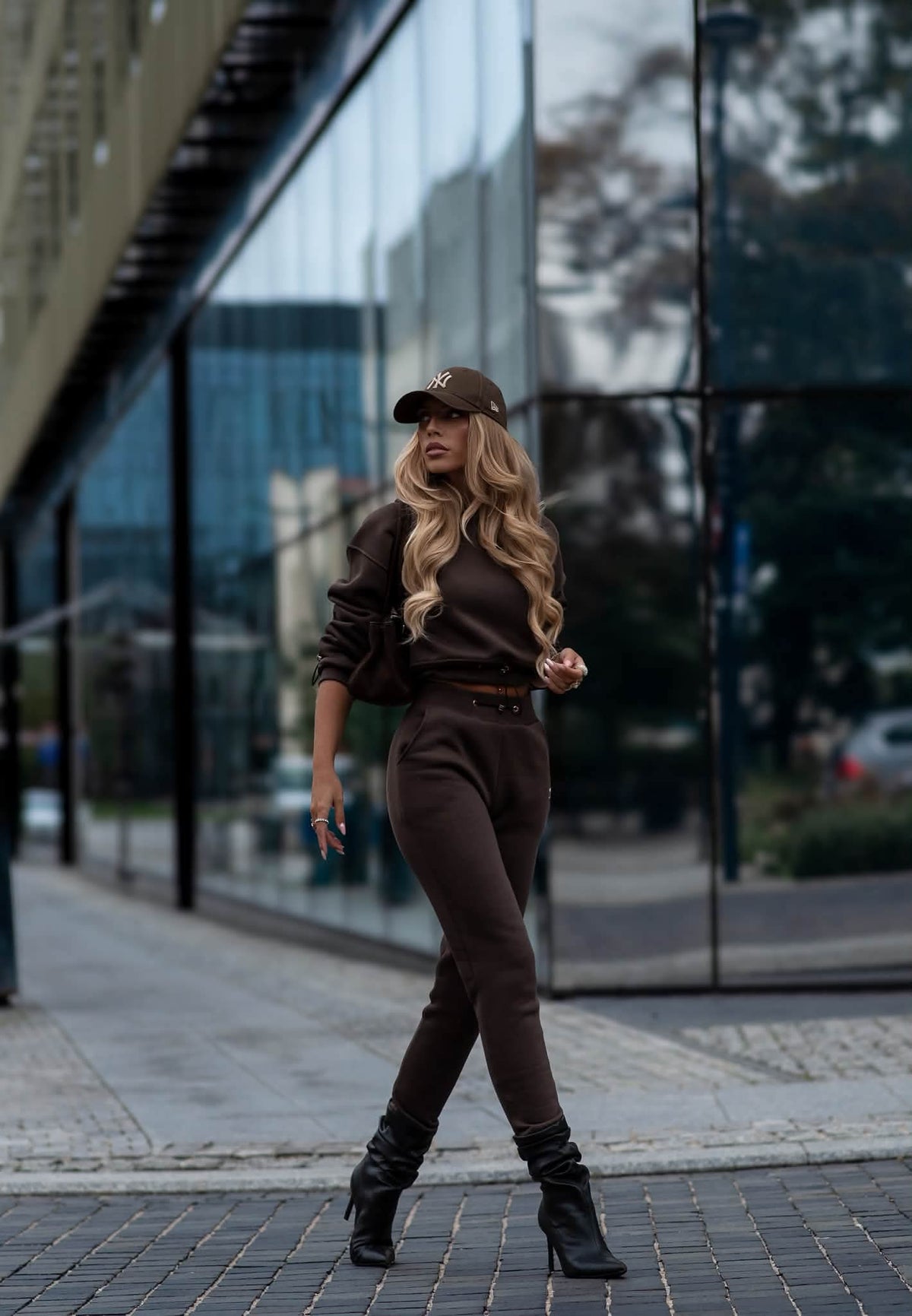 Dame in braunem 2-teiligem Sweat Set, kombiniert mit Cap und schwarzen Stiefeletten im Streetstyle-Look