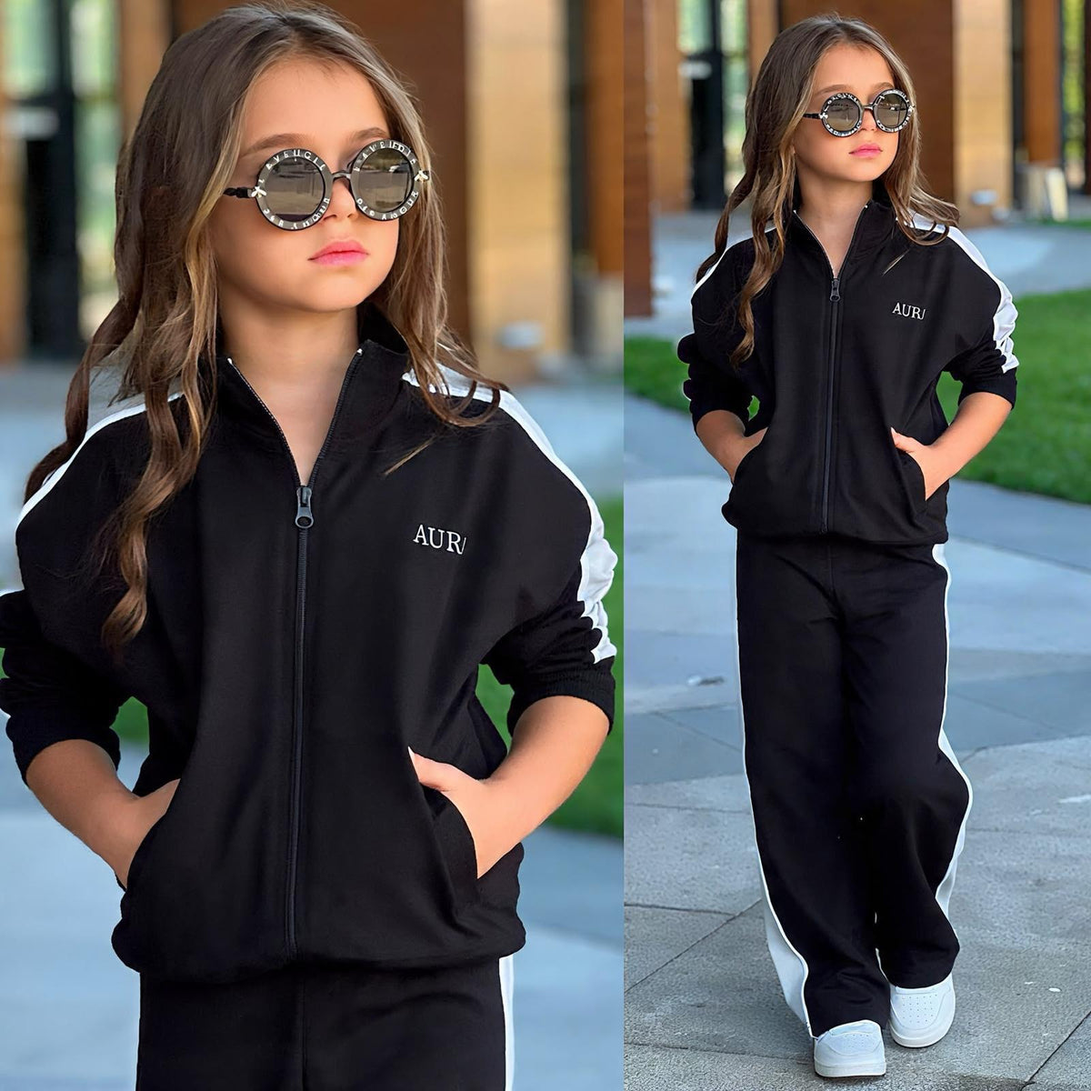 Mädchen im schwarzen AURA Kids Trainingsanzug mit hellen Kontraststreifen, Jackentaschen und weit geschnittener Hose