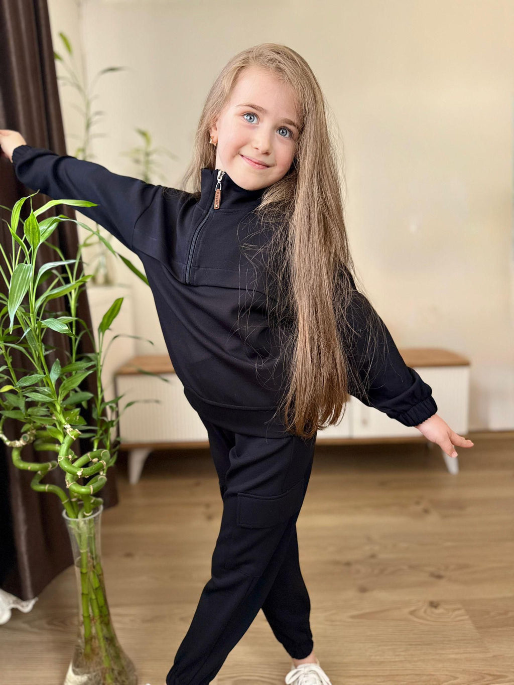 Mädchen trägt ein schwarzes Unisex-Cargo-Set mit Zipper-Sweatshirt, Stehkragen und passender Hose