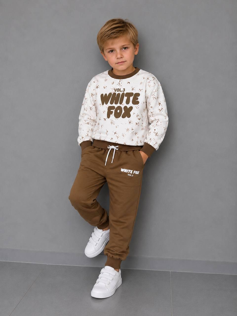 Junge trägt ein Jungen-Set mit WHITE FOX Print, hellem gemustertem Sweatshirt mit braunen Bündchen und brauner Jogginghose mit Kordelzug.