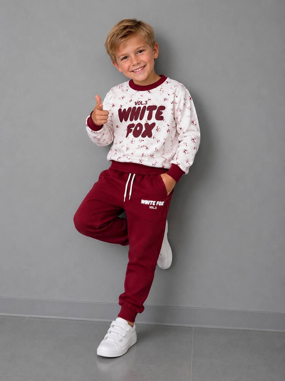 Junge zeigt ein Jungen-Set mit WHITE FOX Print, hellem gemustertem Sweatshirt mit bordeauxfarbenen Bündchen und passender Jogginghose.