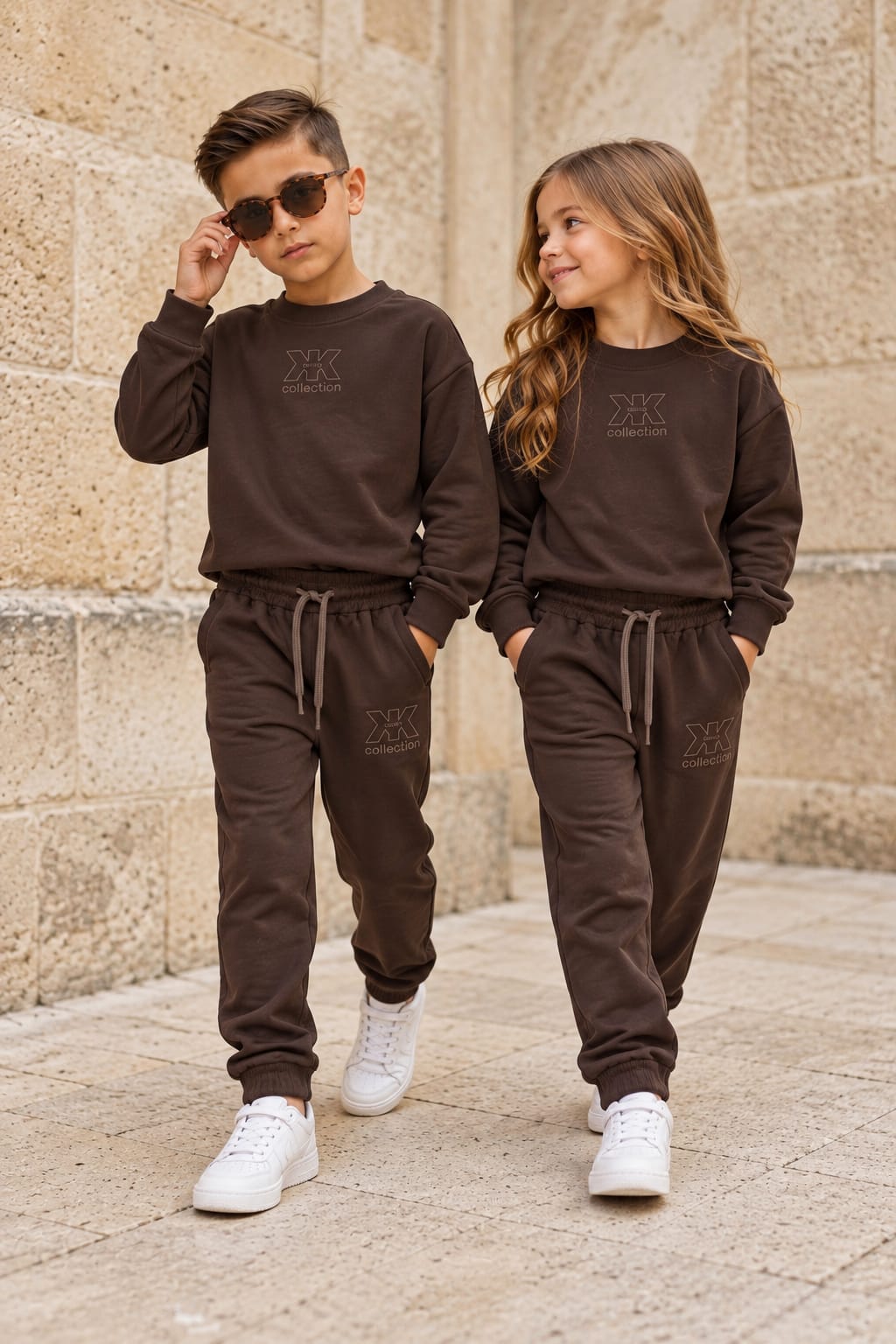 Junge und Mädchen tragen schokobraune X Collection Trainingsanzüge mit Sweatshirt, Logo und passender Hose mit Kordelzug