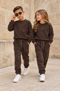 Junge und Mädchen tragen schokobraune X Collection Trainingsanzüge mit Sweatshirt, Logo und passender Hose mit Kordelzug