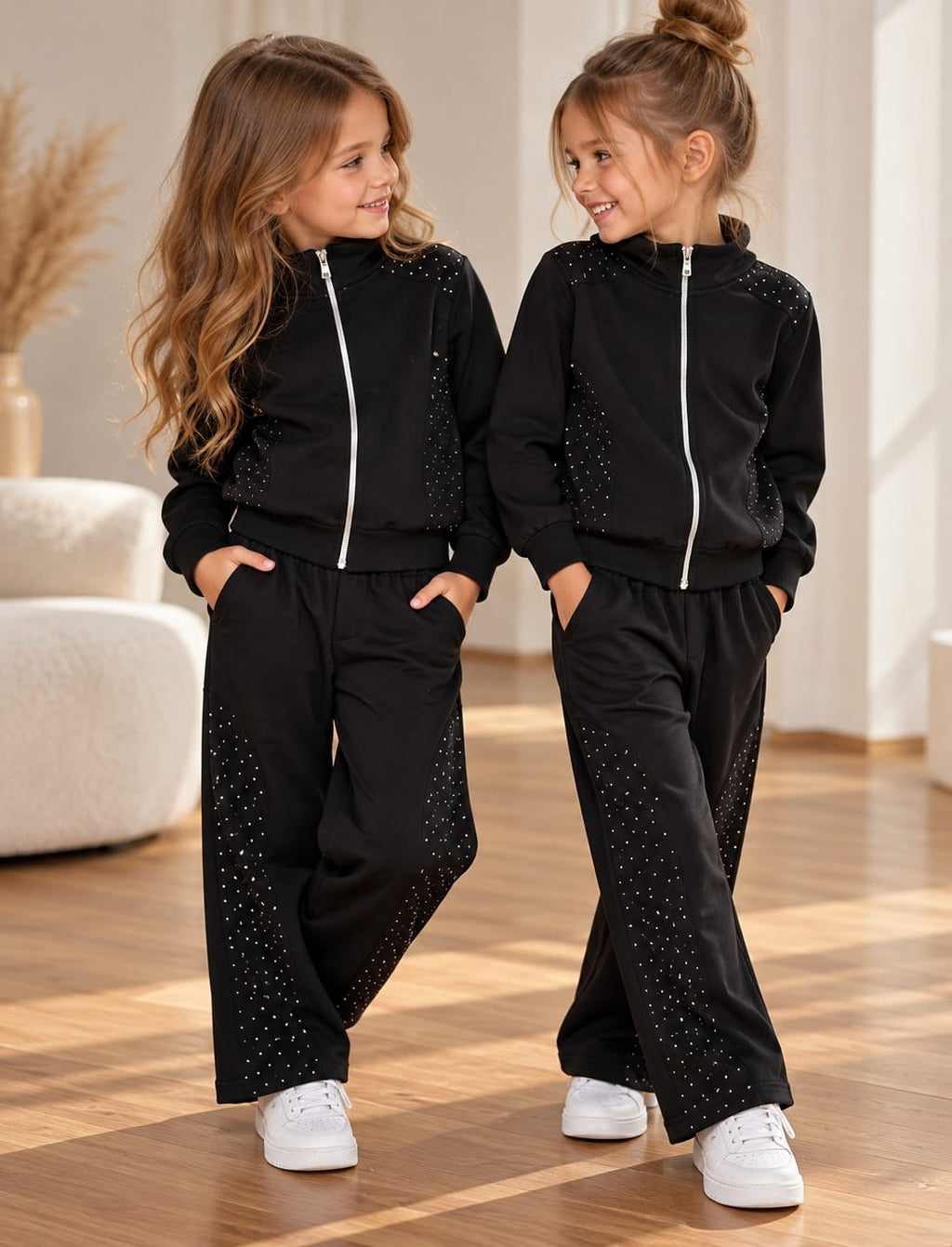 Zwei Mädchen tragen schwarze Sparkle Black Trainingsanzüge mit Glitzer-Details, Sweatjacken mit Reißverschluss und leicht ausgestellten Hosen