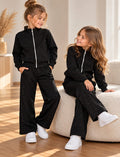 Sparkle Black Mädchen-Set in Schwarz mit Glitzer-Details an Jacke und Hose, gezeigt an einem stehenden und einem sitzenden Mädchen