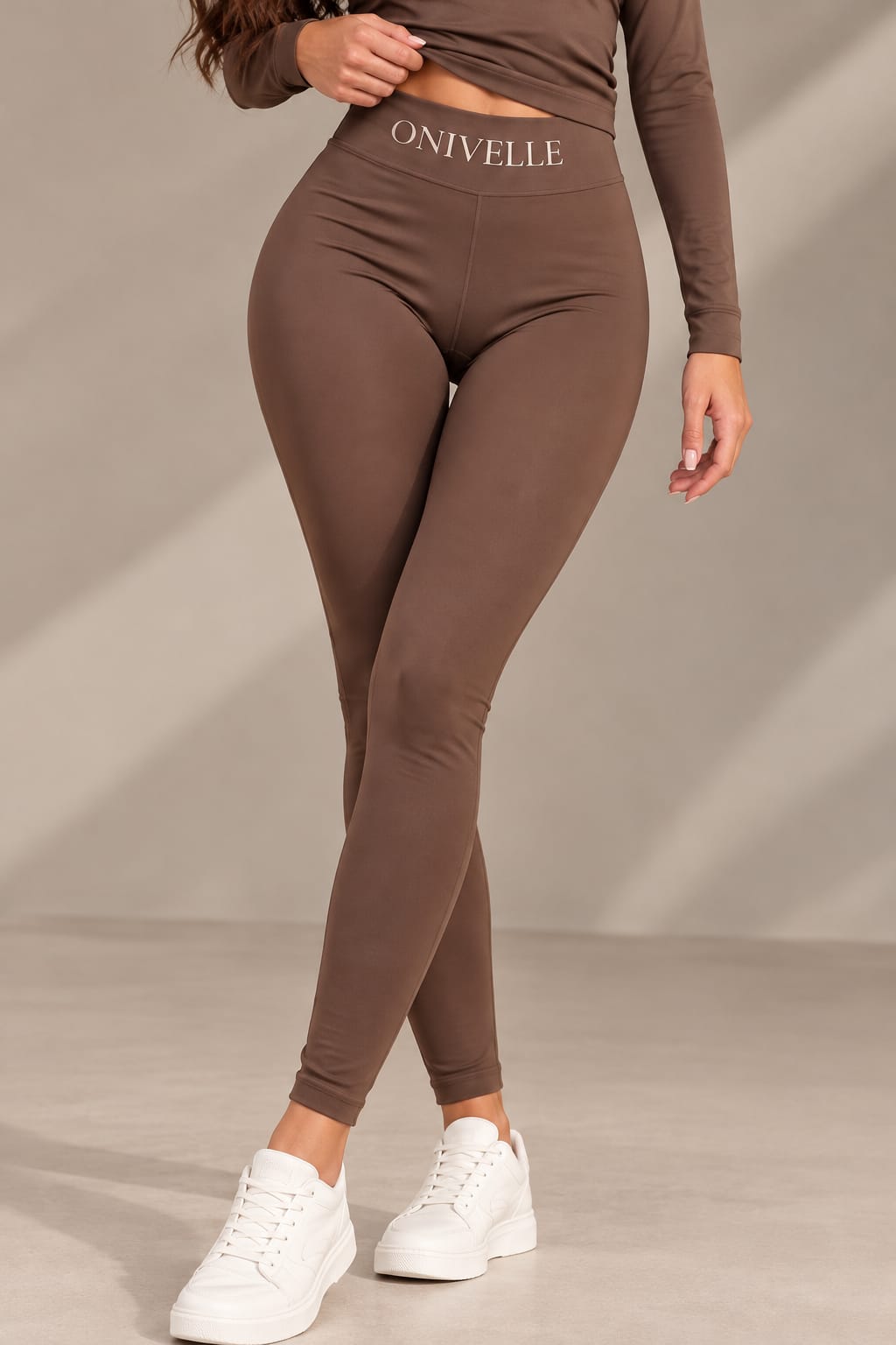 ONIVELLE High-Waist-Leggings in Braun mit breitem Bund und Schriftzug, Vorderansicht am Model mit weißen Sneakern.