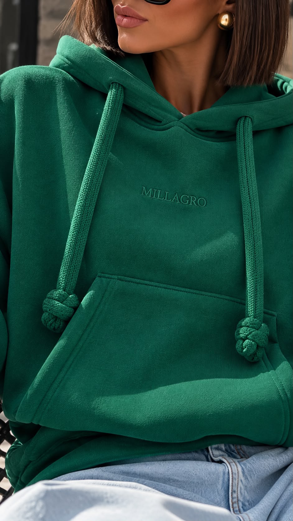 Nahaufnahme des grünen MILLAGRO MONROU Hoodies mit dezentem Brustlogo, Kapuze und geknoteten Kordelenden.
