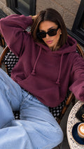 MILLAGRO MONROU Damen-Hoodie in Pflaume mit Kapuze, Kängurutasche und dezentem Brustlogo, getragen mit heller Jeans.