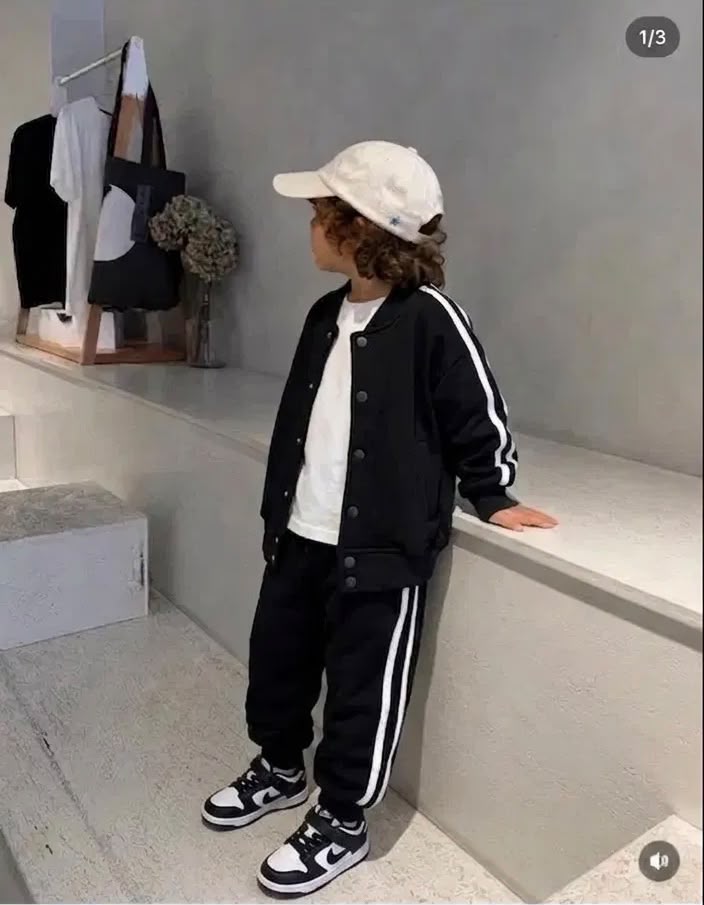 Schwarzes Kinder-Set am Model mit offener Collegejacke, weißem T-Shirt und Jogginghose mit weißen Kontraststreifen