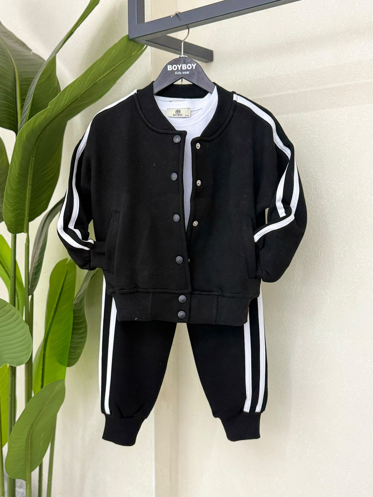 Schwarzes dreiteiliges Kinder-Set auf einem Kleiderbügel mit Collegejacke, weißem T-Shirt und Jogginghose