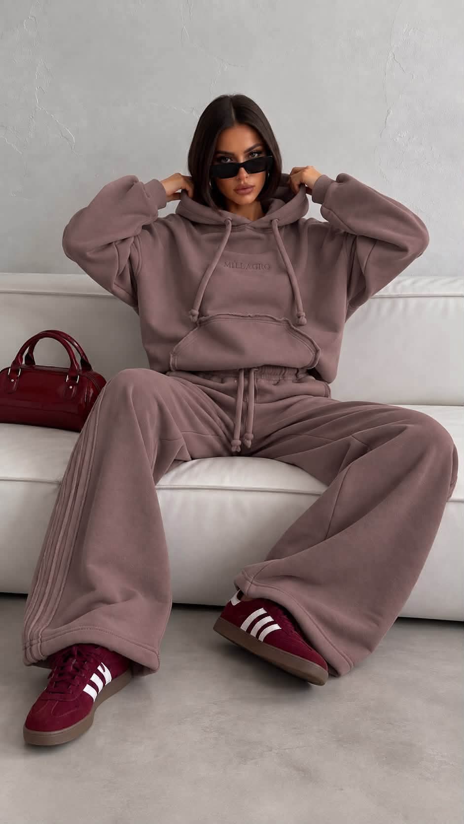 MILLAGRO Milano Oversize-Jogginganzug in Fango mit Kapuze, Kängurutasche und weit geschnittener Hose, sitzend gezeigt.