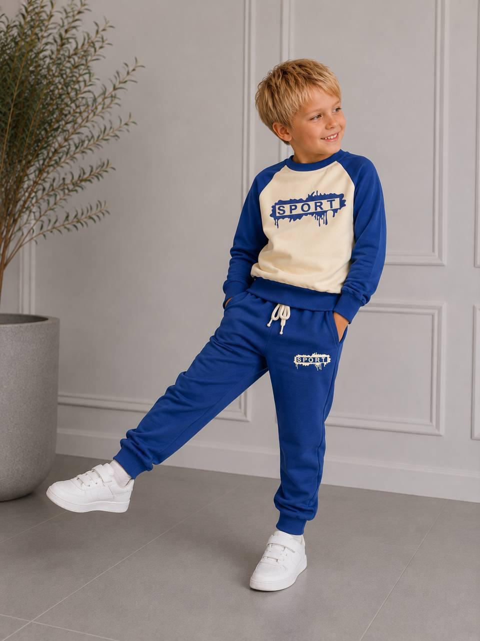 Junge trägt das blau-cremefarbene Happy Street Set mit Raglanärmeln, SPORT-Print und blauer Jogginghose mit Kordelzug.