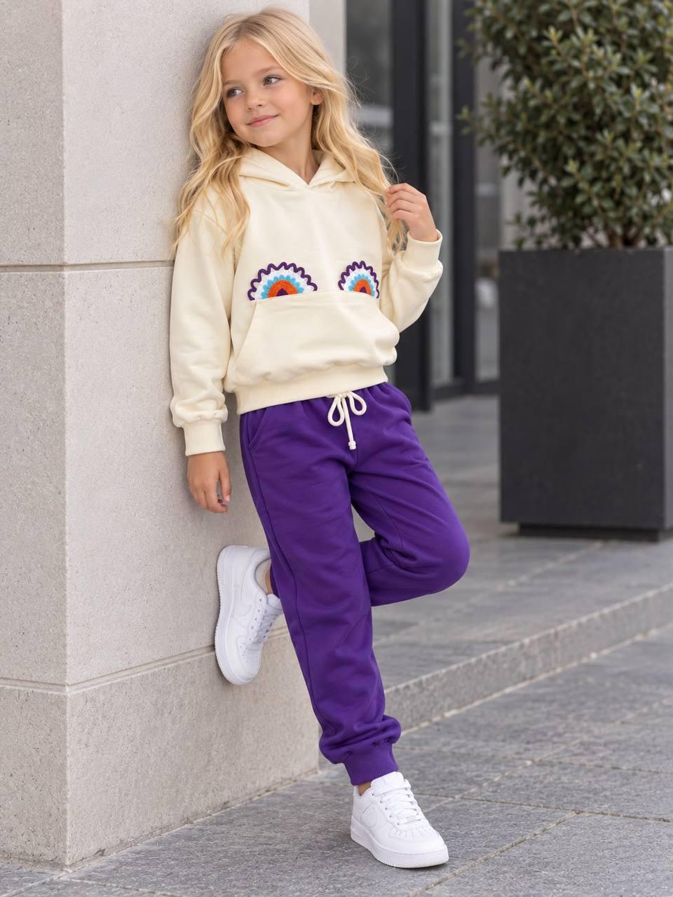 Rainbow Love Mädchen-Set mit cremefarbenem Kapuzenoberteil und dunkellila Hose mit Bündchen, an einem Mädchen gezeigt.