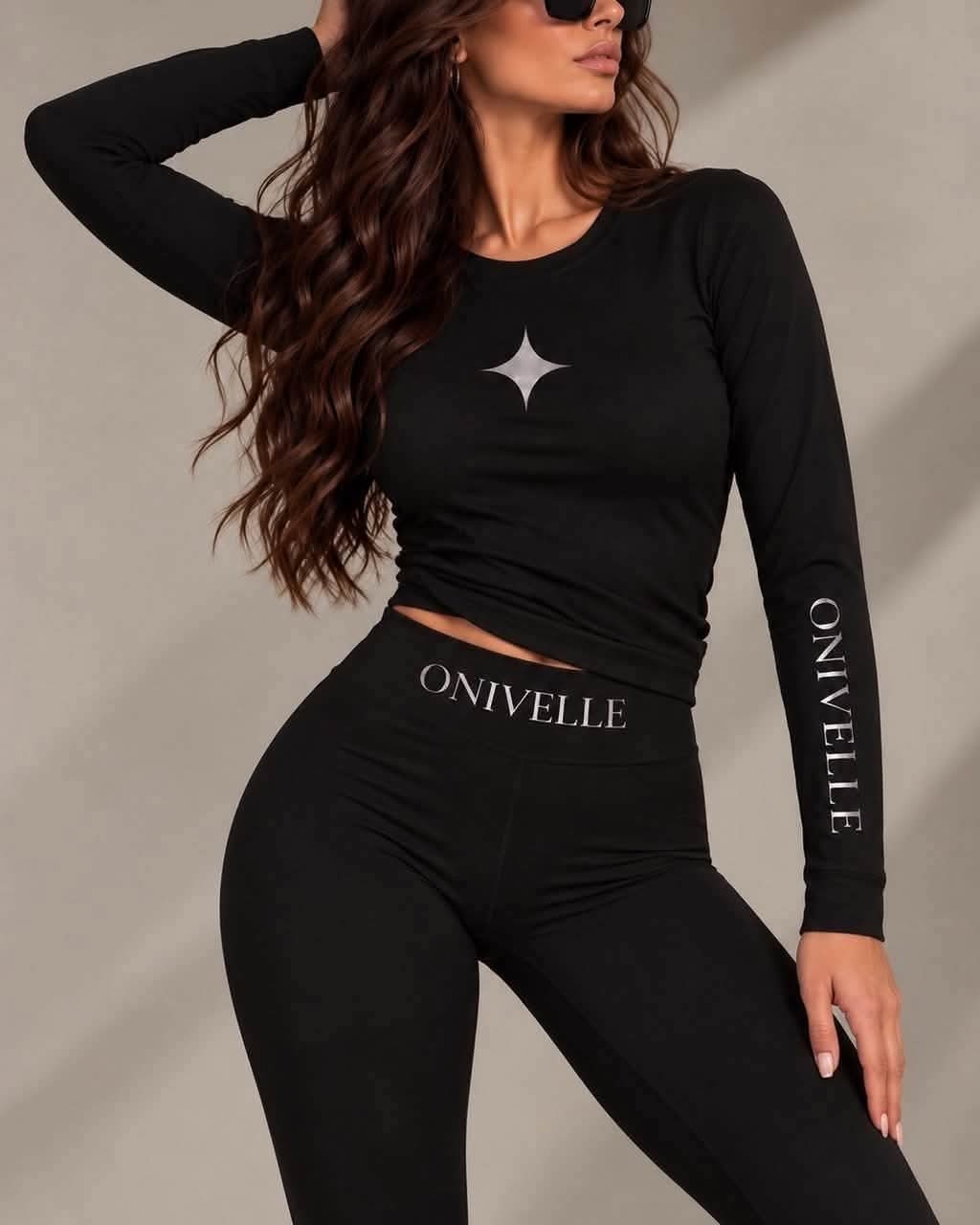 Figurbetontes ONIVELLE Damen-Langarmshirt in Schwarz mit Sternmotiv und Schriftzug am Ärmel, am Model mit passender Leggings.