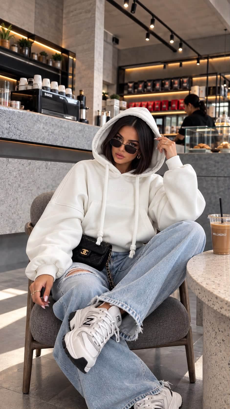 MILLAGRO MONROU Hoodie in Weiß mit Kapuze und Kängurutasche, an einem sitzenden Model mit Jeans und Sneakern.