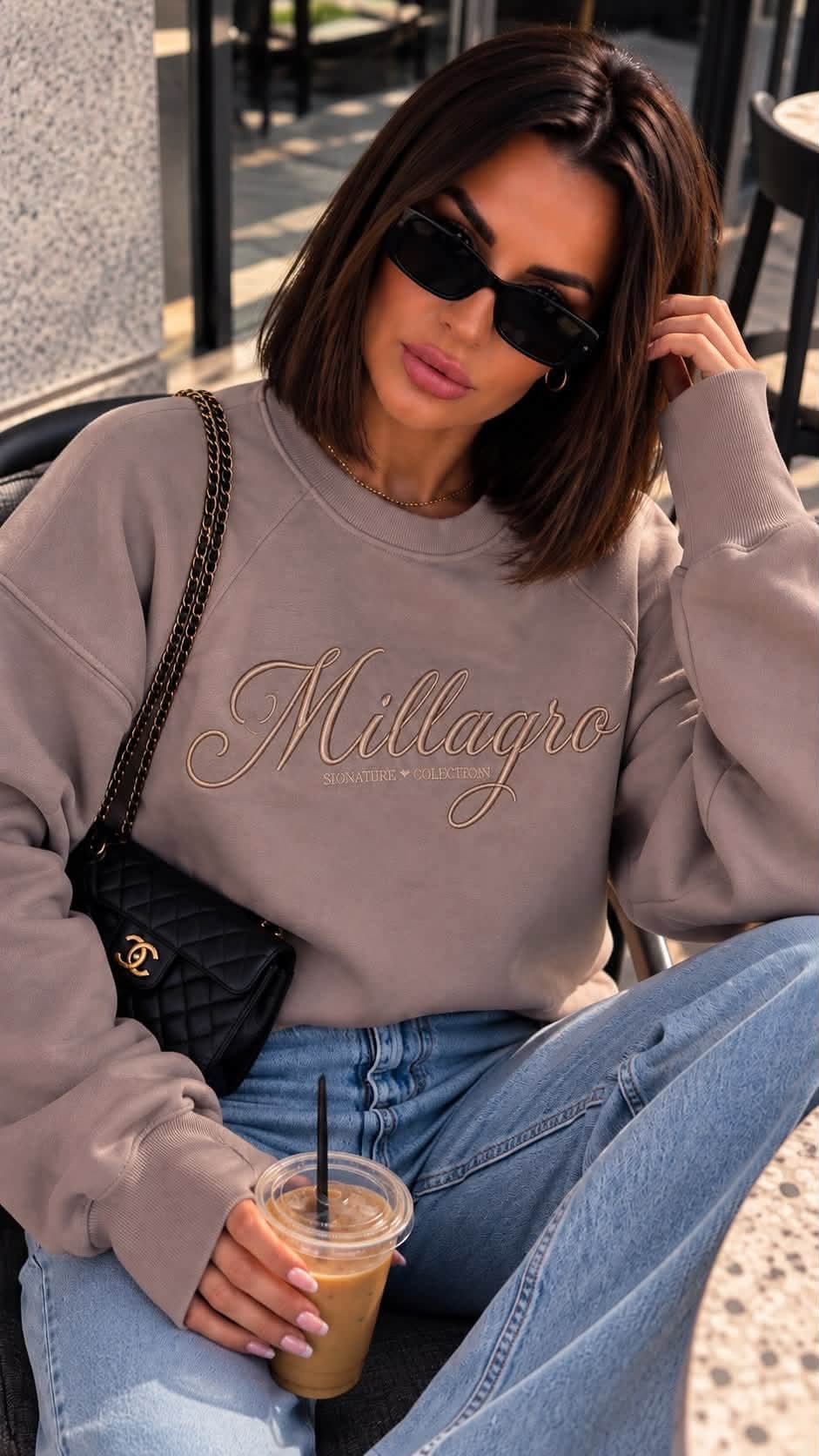 MILLAGRO Damen-Sweatshirt in Taupe mit tonaler Logo-Stickerei und geripptem Rundhalsausschnitt, getragen mit Jeans.