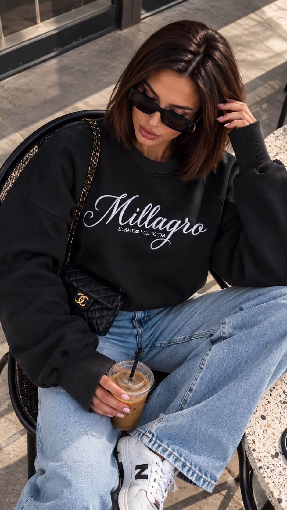 MILLAGRO Damen-Sweatshirt in Schwarz mit weißer Logo-Stickerei und langen Ärmelbündchen, sitzend gezeigt