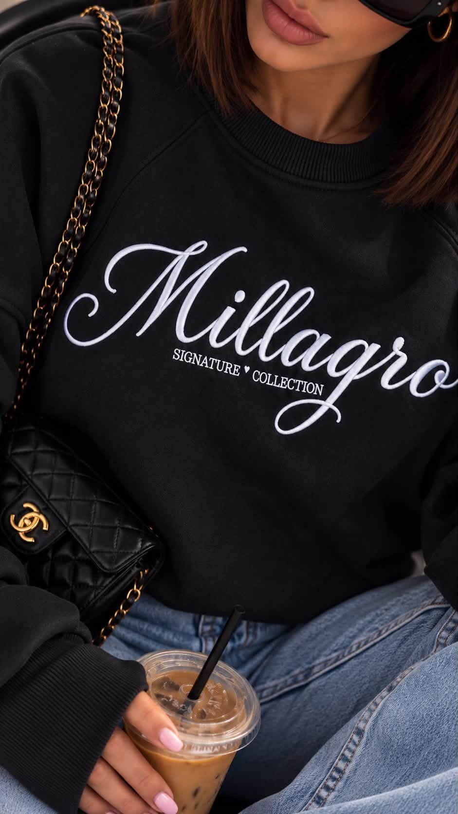 Nahaufnahme der weißen Millagro-Signature-Collection-Stickerei auf dem schwarzen Damen-Sweatshirt.