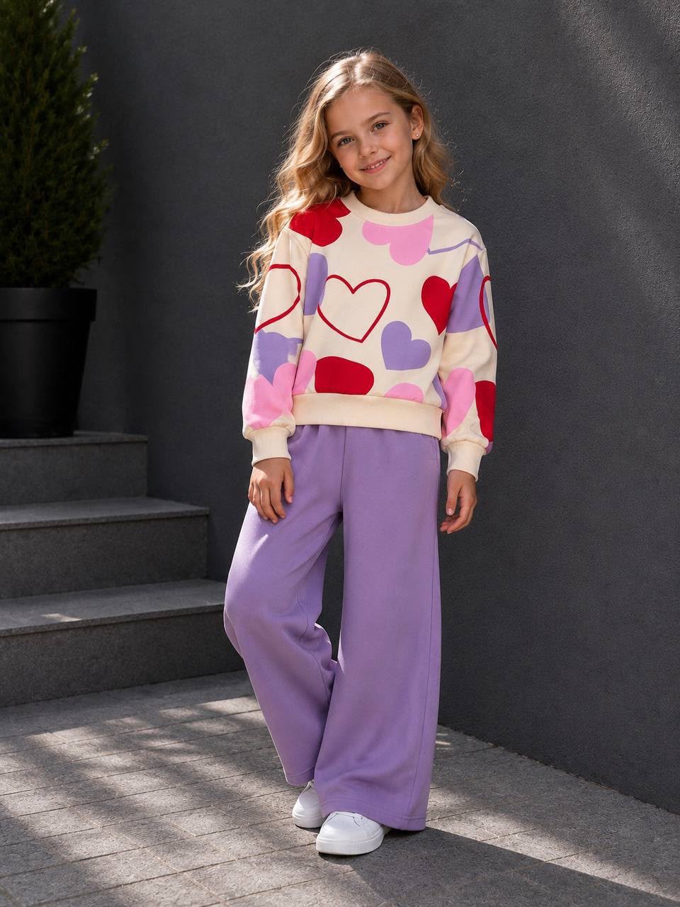 Mädchen trägt ein zweiteiliges Outfit mit Herz-Print-Sweatshirt und lila weiter Hose