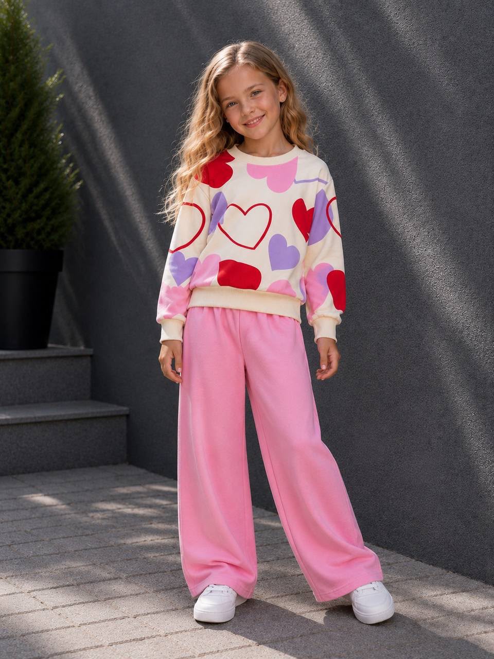 Mädchen trägt ein zweiteiliges Outfit mit Herz-Print-Sweatshirt und rosafarbener weiter Hose